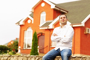 A man sitting on a rock wall in front of a house