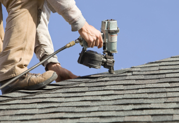 A roofer with a nail gun installing new shingles.